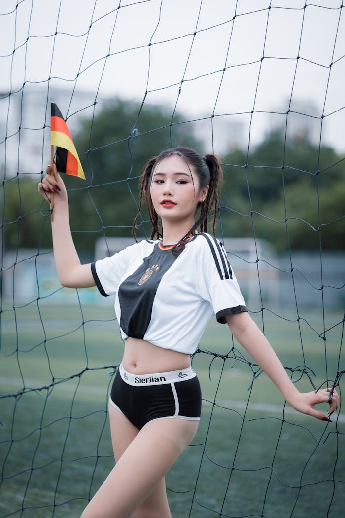 A young woman in sports attire poses on a football field, holding a flag.