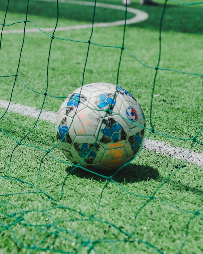 Close-up of a soccer ball resting on green turf with net, ideal for sports themes.