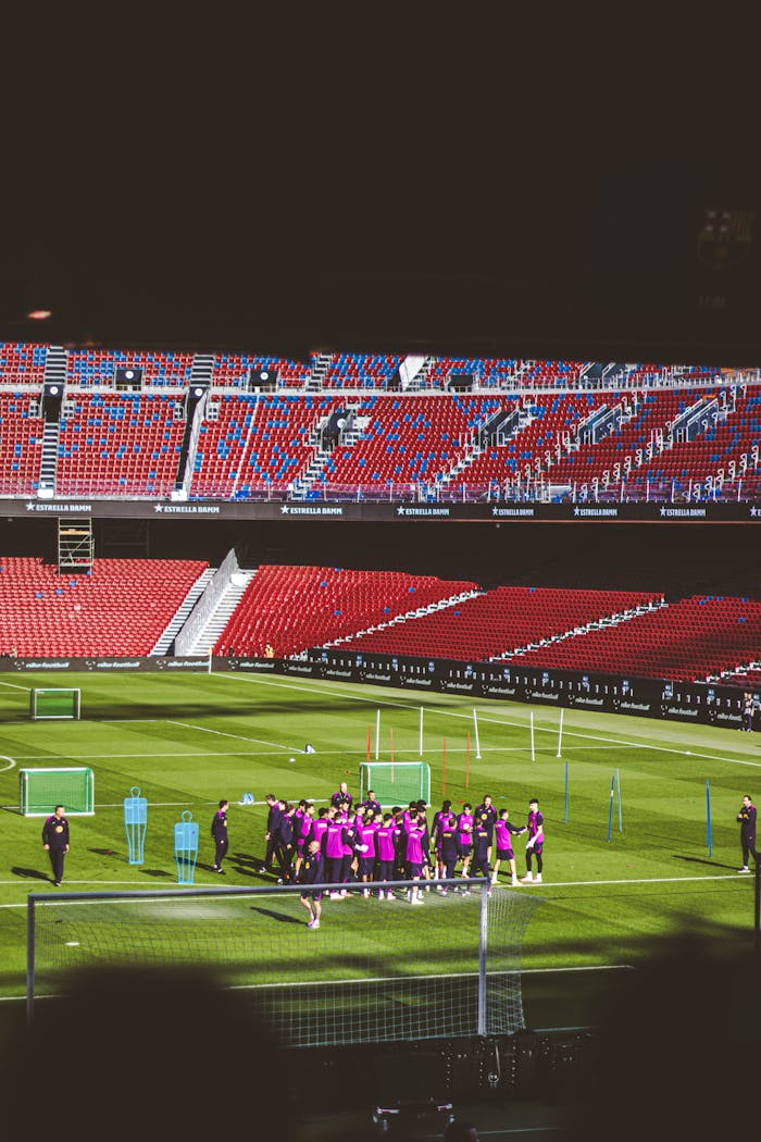 A soccer team practices on a green field inside an empty stadium.