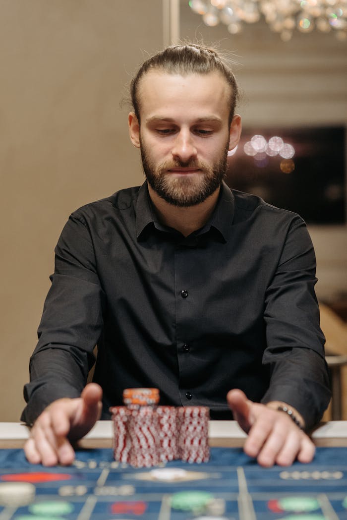 Man with beard sitting at casino table, focused on placing bets with gaming chips.
